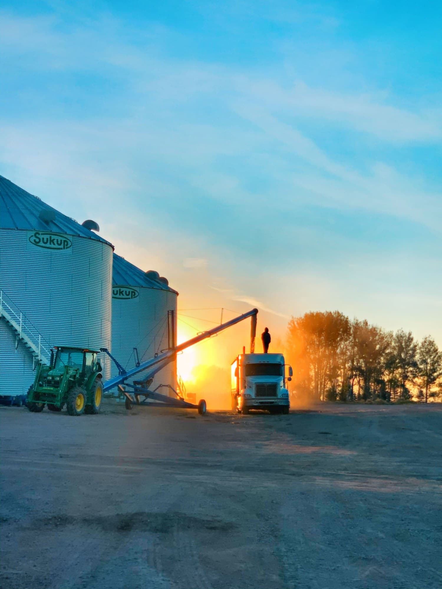 Grain bins, tractor, and truck loading out at sunset